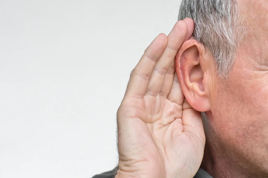 close up of an older man holding his hand up to his ear due to hearing loss
