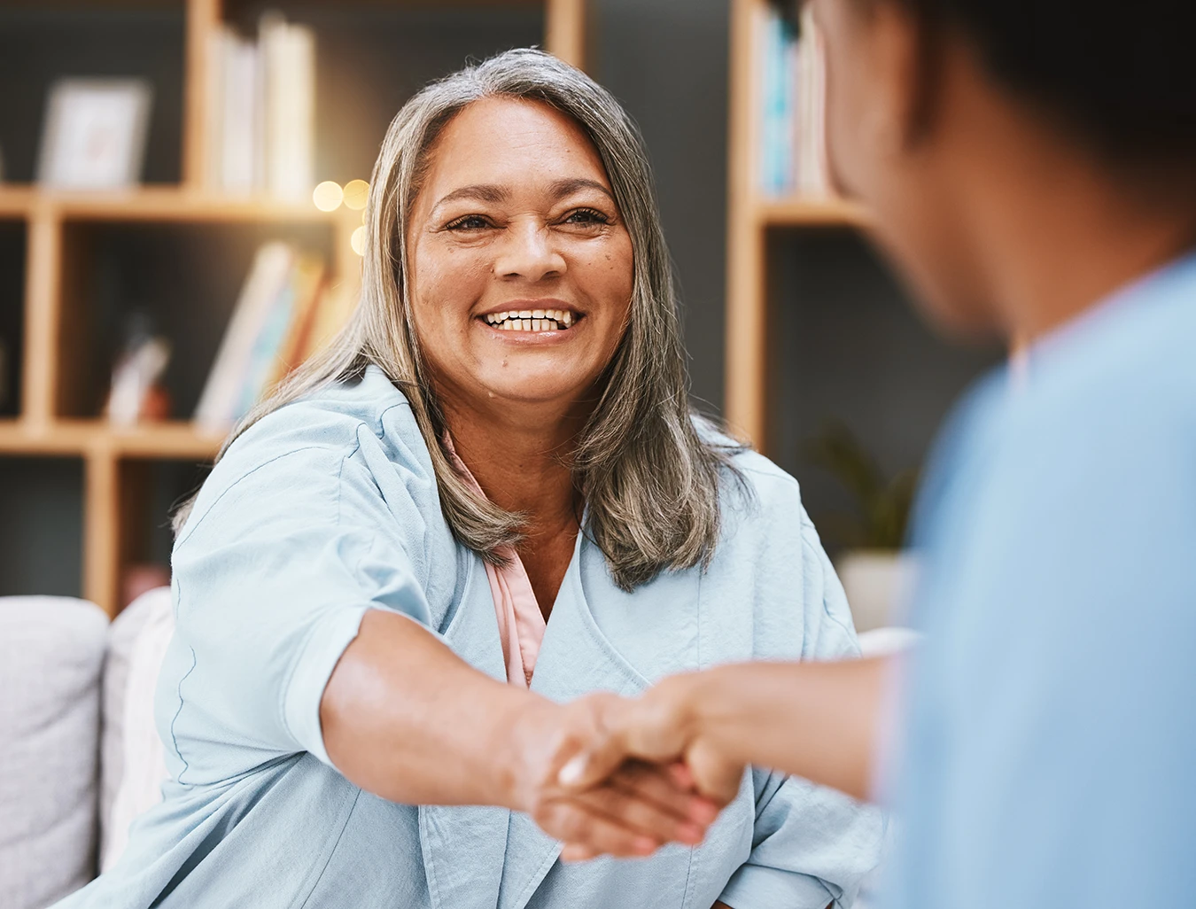 An older adult woman at an audiology clinic, smiling and shaking hands with an Audiologist
