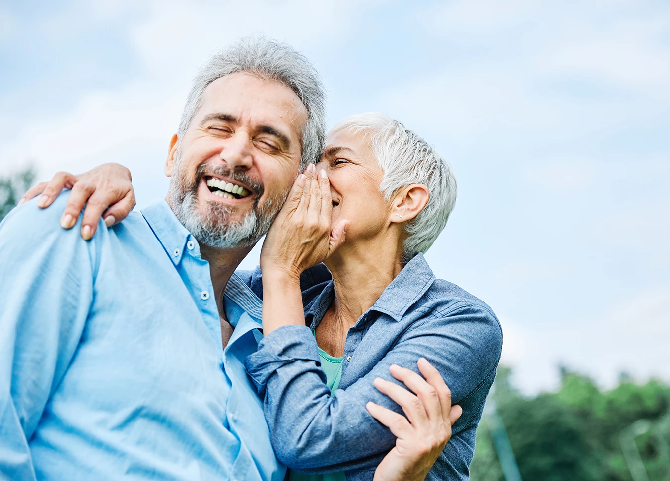 Happy senior couple, man and wife, smiling as the woman holds her hand up to the mans ear as if to whisper a secret, symbolising the best hearing aid brands for seniors.
