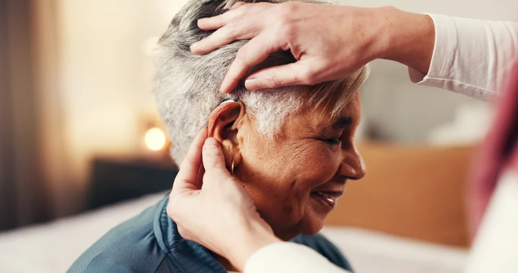 An audiologist gently helping a senior woman put in her behind-the-ear BTE hearing aid, symbolising the best hearing aid brand for seniors.