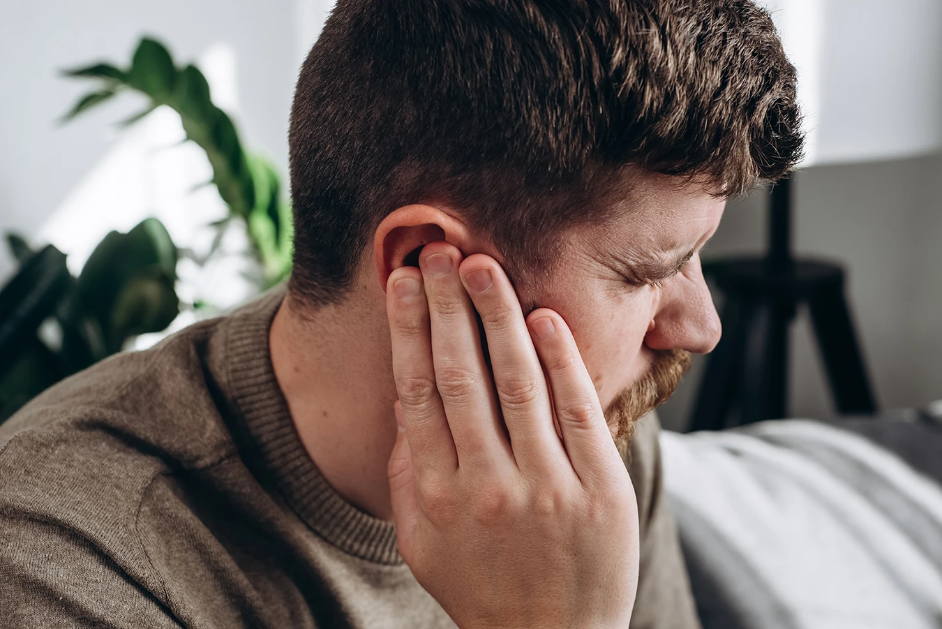 Close-up of a young, bearded, caucasian man, touching ear, suffering from tinnitus ear ringing.